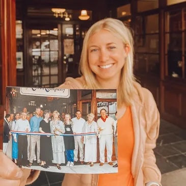 Woman holding a photo of a group of people in front of The Coffee Company doing the ribbon cutting. 