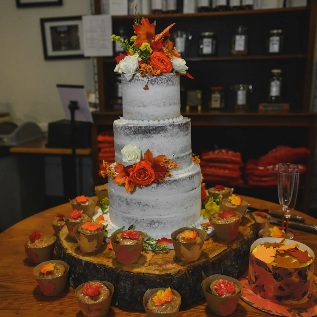 Multi-tiered wedding cake with floral decorations on a wooden stand, surrounded by cupcakes.