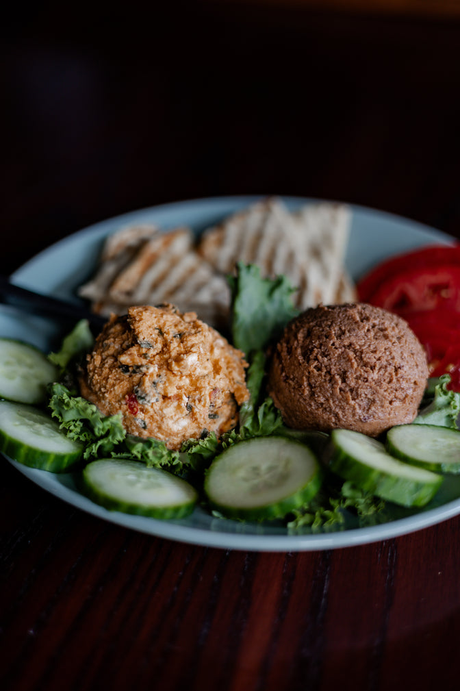 Plated dish with feta dip, bean dip, cucumber, tomato, and pita on a dark background