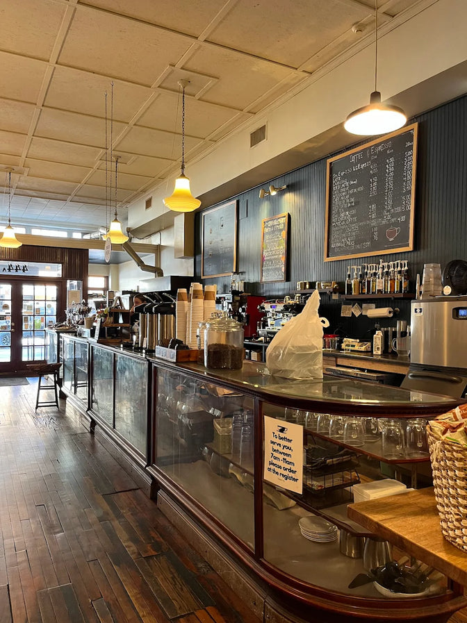Interior of a coffee shop with a counter, shelves, and a chalkboard menu.