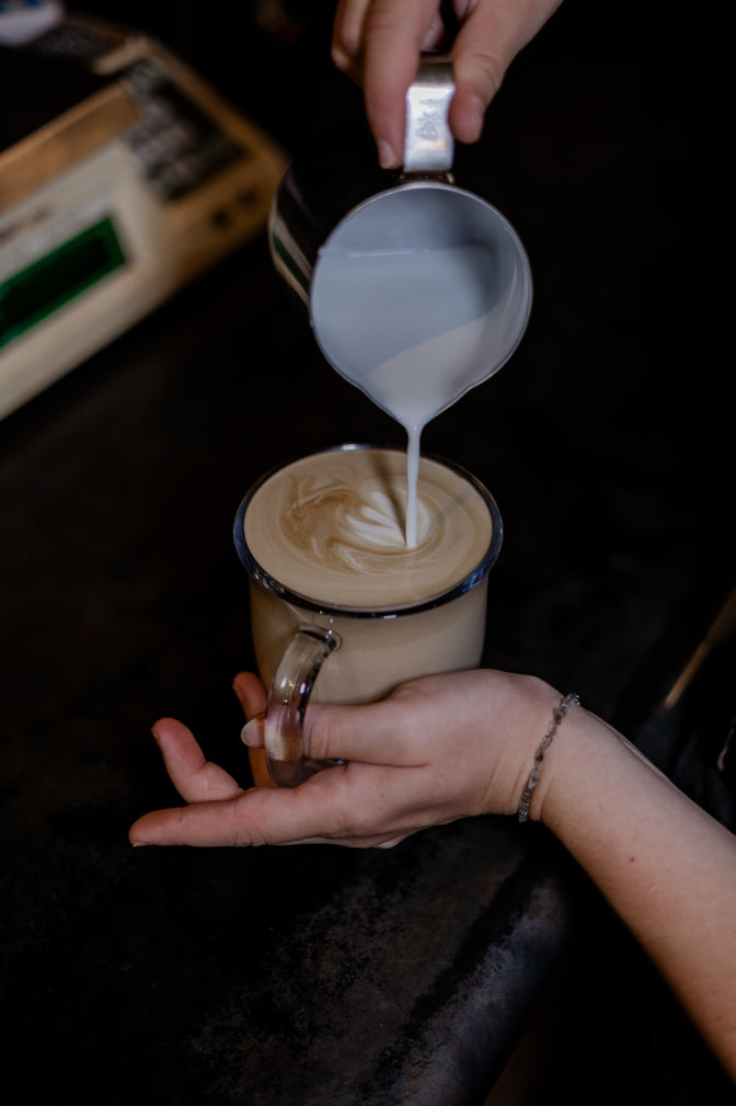 Person pouring milk into a coffee cup on a dark surface