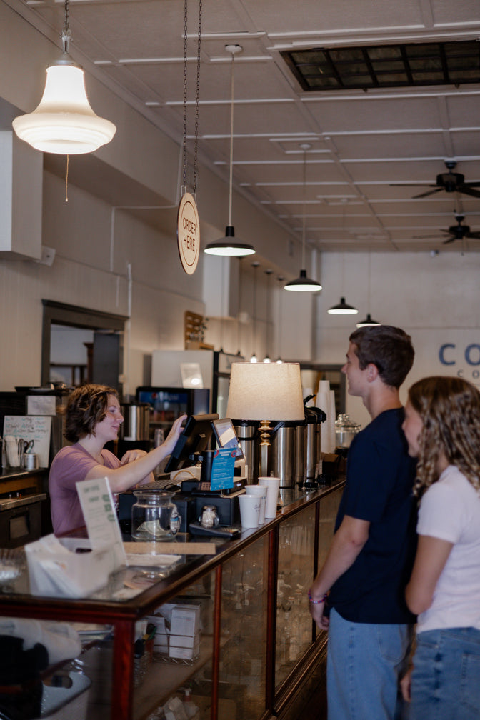 People standing at a counter in a coffee shop with a barista behind the counter.